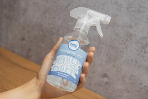 bottiglia di detergente vetri con etichetta blu e spruzzino in mano
